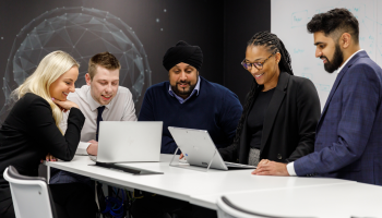Group of people look at laptops in office