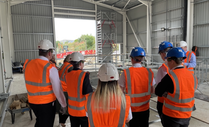 A mixed group of young adults look are shown the Gosforth Depot site by the construction team wearing orange high vis and helmets