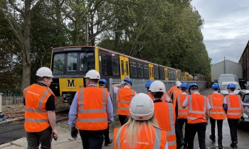 A mixed group of young adults look are shown the Gosforth Depot site by the construction team wearing orange high vis and helmets